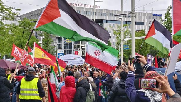 Menschenmenge mit palästinensischen und iranischen Fahnen bei einer Demonstration in einer Stadt.