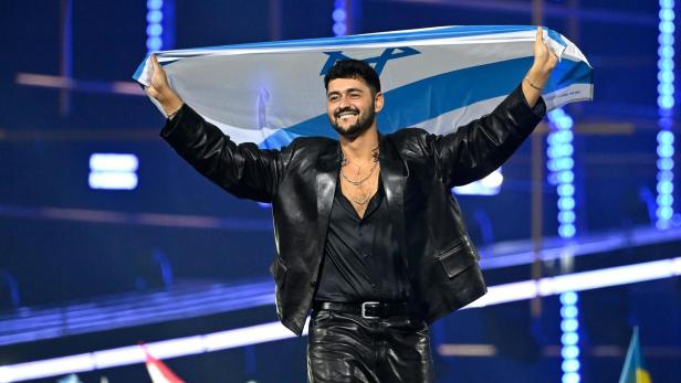 Ein Mann in Leder hält lächelnd eine israelische Flagge hoch.