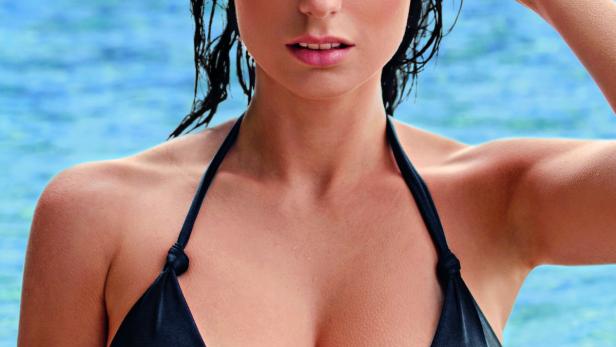 Eine Frau mit nassen Haaren und einem schwarzen Bikini vor blauem Wasser.