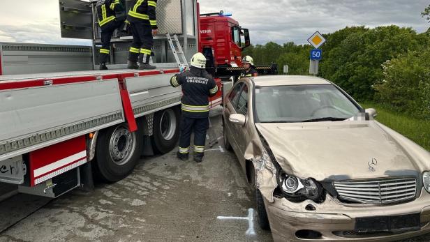 Mehrere Feuerwehrleute sichern ein beschädigtes Auto neben einem Einsatzfahrzeug auf einer Landstraße.