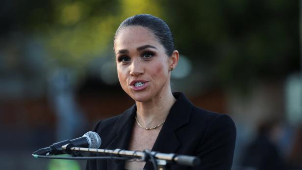 Meghan, Herzogin von Sussex, spricht in einem schwarzen Blazer vor einem Mikrofon.
