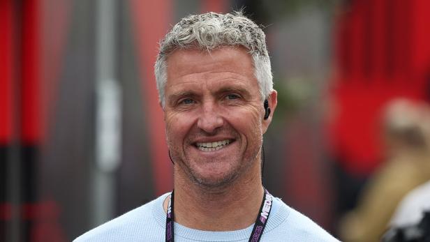 Ralf Schumacher lächelt mit einem Akkreditierungsband um den Hals bei einer öffentlichen Veranstaltung.
