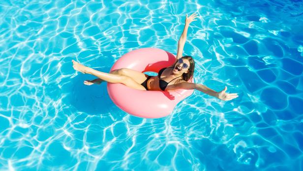 Eine lachende Frau entspannt auf einem pinken Schwimmring im Pool.