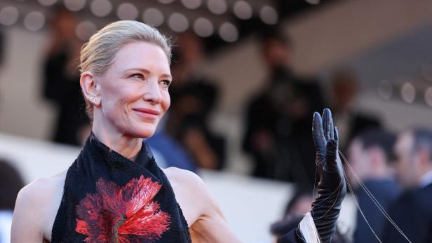 Cate Blanchett lächelt und winkt mit einem schwarzen Handschuh mit Fäden.
