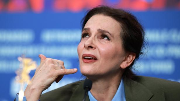Eine Frau mit blauem Hemd und grünem Blazer gestikuliert mit der Hand am Mikrofon.