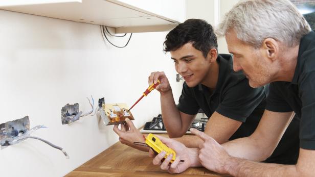 Electrician With Apprentice Working In New Home