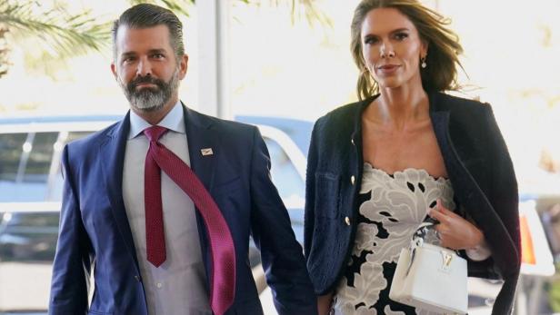Donald Trump Jr im Anzug und Bettina Anderson im Blumenkleid gehen Händchen haltend spazieren.