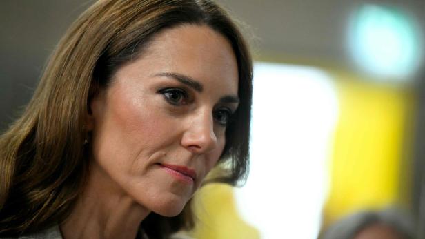 Prinzessin Kate mit langen braunen Haaren blickt nachdenklich zur Seite, im Hintergrund unscharfe Lichter.