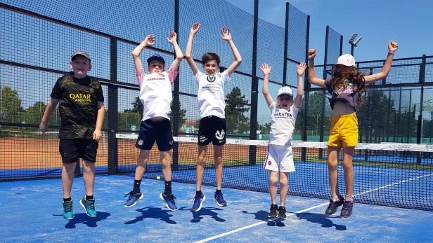 Fünf Kinder springen lachend auf einem Sportplatz in die Luft.