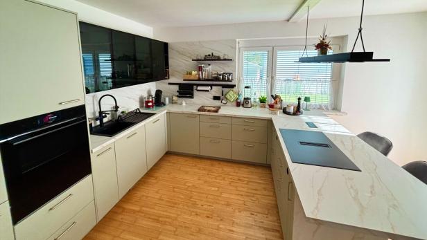 Eine moderne, helle Küche mit großer Arbeitsfläche, schwarzen Akzenten und Fenstern mit Blick ins Grüne.