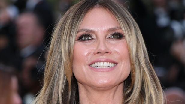 Heidi Klum lächelt mit blonden Haaren und goldenem Kleid mit Spitze.