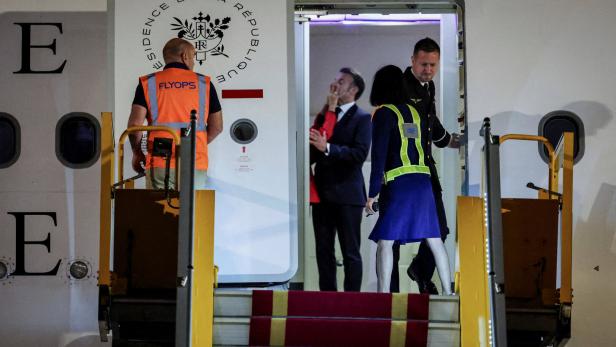 Mehrere Personen stehen an einer Flugzeugtür mit rotem Teppich und Sicherheitswesten, während sie ein- oder aussteigen.