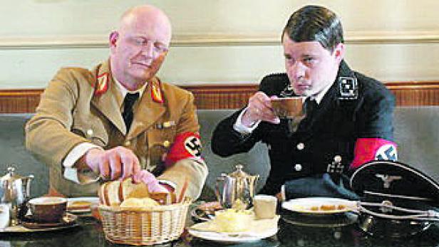 Zwei Männer in Uniformen sitzen an einem Tisch und essen Gebäck.