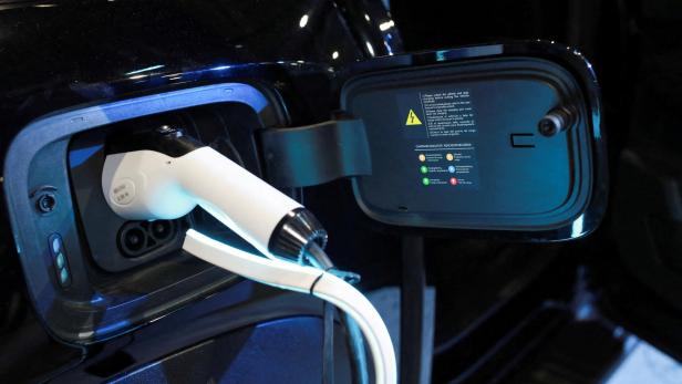 Ein weißes Ladekabel ist an ein schwarzes Elektroauto angeschlossen, die Ladeklappe ist geöffnet.