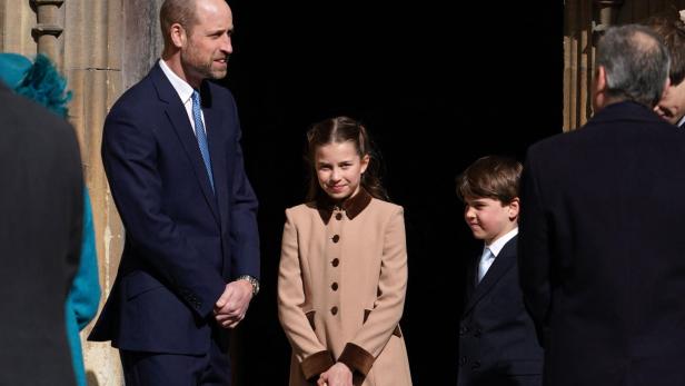 Prinz William steht mit Prinzessin Charlotte und Prinz George vor einem Gebäude.