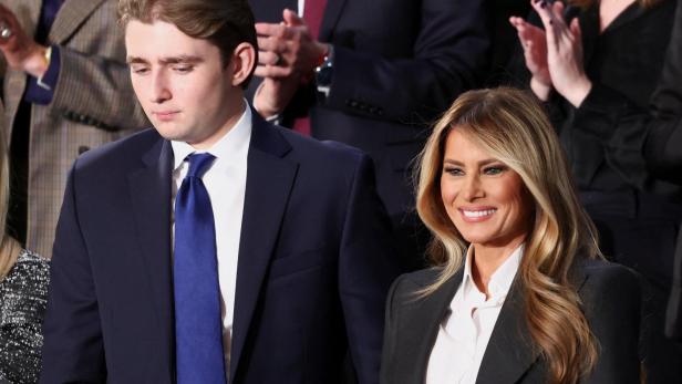 Melania Trump lächelt neben ihrem Sohn Barron mit dunklem Anzug und blauer Krawatte.