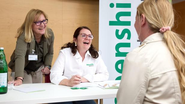 Zwei Frauen führen ein Bewerbungsgespräch mit einer Bewerberin am Tisch bei der Pflegejobbörse.