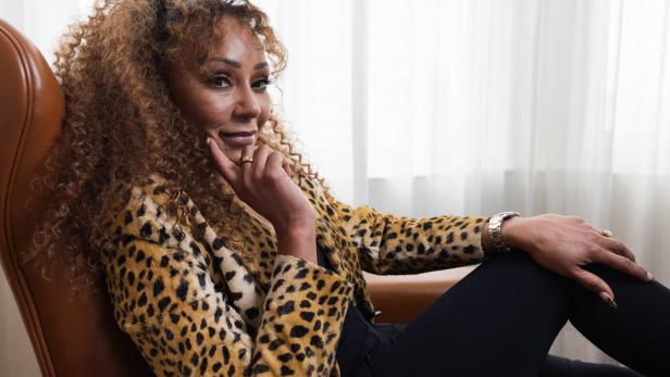 Mel B mit lockigem Haar und Leopardenmuster-Jacke sitzt in einem Sessel.