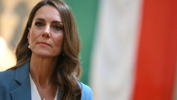 Prinzessin Kate mit braunen, gewellten Haaren und blauem Blazer schaut zur Seite.