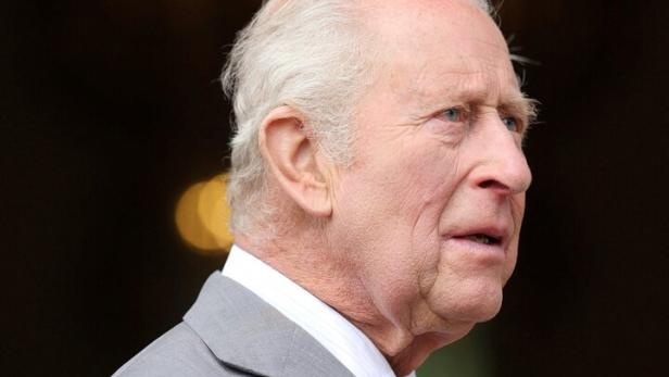 König Charles III. im grauen Anzug, mit hellem Haar und Krawatte, blickt nach rechts.