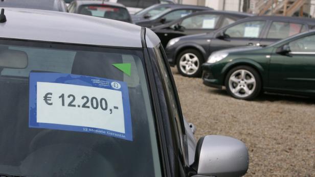 Mehrere Gebrauchtwagen stehen auf einem Parkplatz, eines davon ist für 12.200 Euro mit 12 Monaten Garantie ausgezeichnet.