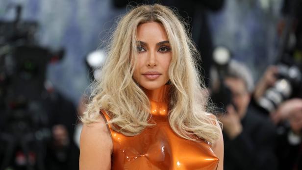 Kim Kardashian trägt ein orangefarbenes Kleid und blondes, gewelltes Haar.
