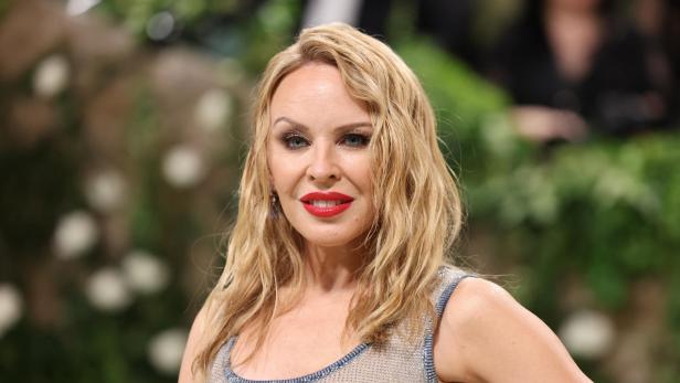 Kylie Minogue lächelt mit rotem Lippenstift und blonden, gewellten Haaren.