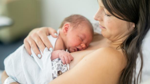 Das Bild zeigt ein Neugeborenes, das auf der Brust seiner Mutter liegt und schläft.
