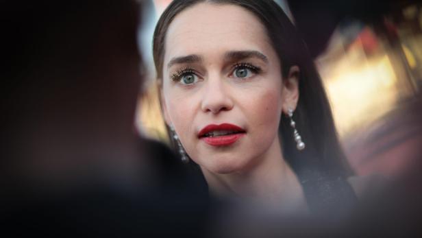 Emilia Clarke mit roten Lippen und Ohrringen schaut aufmerksam zur Seite.