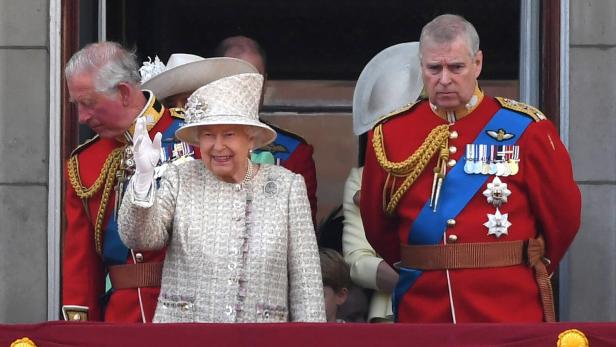 Königin Elisabeth II. winkt, flankiert von Prinz Charles und Prinz Andrew in Uniformen.