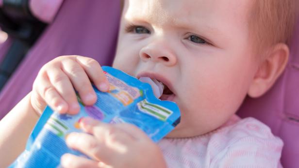 Ein Baby hält einen blauen Quetschbeutel und trinkt daraus.