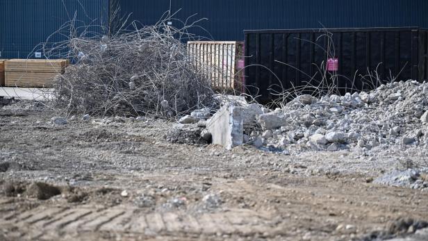 Baustellenhof mit Schutt, Drahtresten und Containern vor einer blauen Halle.