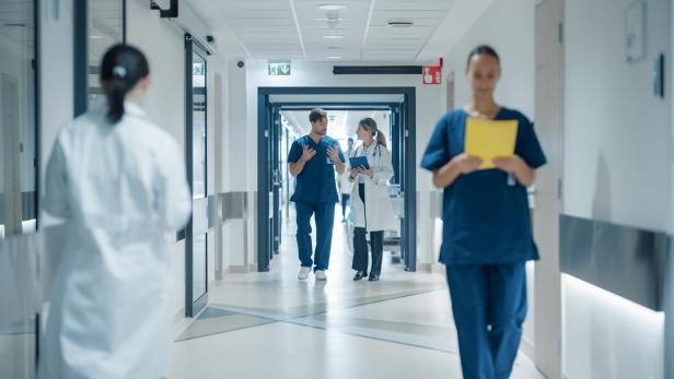 Mehrere medizinische Fachkräfte gehen und unterhalten sich in einem hellen Krankenhausflur.