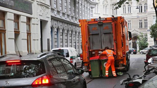 Ein Müllwerker in orangefarbener Arbeitskleidung leert Mülltonnen in ein orangefarbenes Müllfahrzeug auf einer Straße.