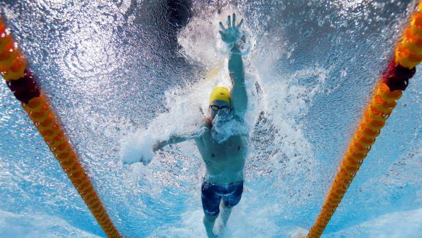 Ein Schwimmer mit gelber Badekappe schwimmt kraulend zwischen zwei gelben Bahnleinen unter Wasser.