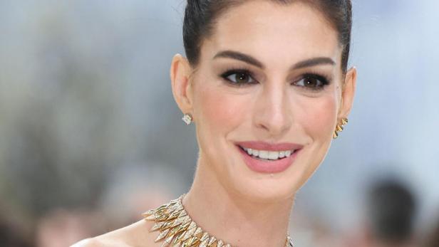 Anne Hathaway. mit hochgesteckten Haaren trägt ein schulterfreies Kleid mit schwarz-weißem Muster und eine auffällige goldene Halskette.