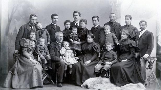 Eine große Familie posiert in altmodischer Kleidung für ein Schwarzweiß-Gruppenporträt.