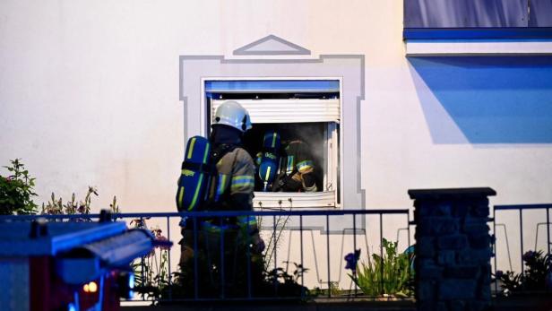 Zwei Feuerwehrleute mit Atemschutzgeräten steigen durch ein geöffnetes Fenster in ein verrauchtes Gebäude ein.