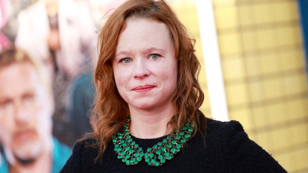Thora Birch mit roten Haaren und einer grünen Halskette lächelt in die Kamera.