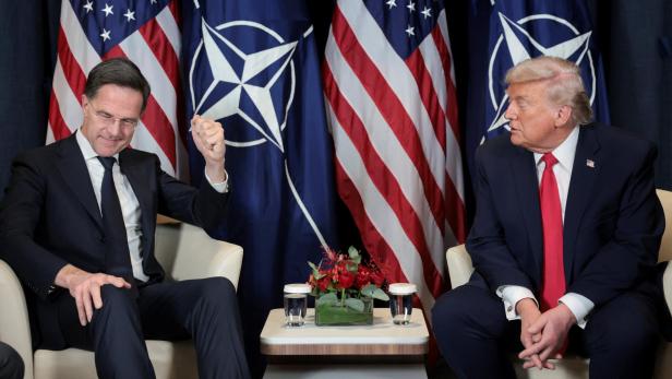 Mark Rutte gestikuliert neben Donald Trump vor US- und NATO-Flaggen.