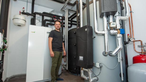 Ein Mann steht in einem Technikraum neben einer modernen Heizungsanlage mit vielen Rohren und Speichern.