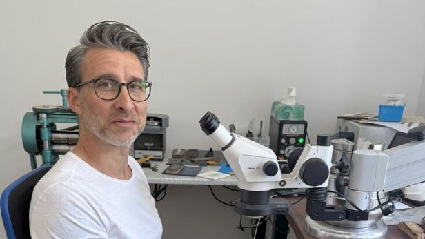 Armin Bundschuh sitzt an einem Arbeitstisch mit Mikroskop und Werkzeugen und arbeitet konzentriert an einem kleinen Objekt.