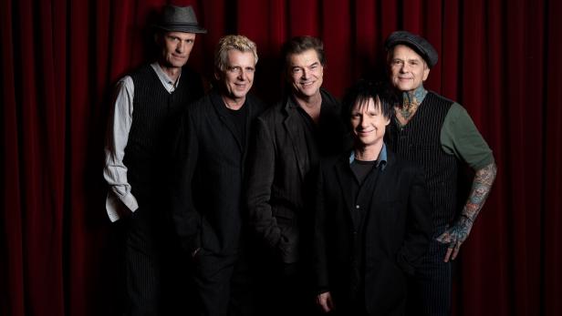 Die Toten Hosen posieren vor einem roten Vorhang, einige tragen Hüte und Anzüge.