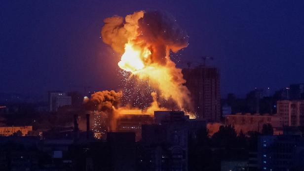 Große Explosion mit Feuerball und Rauchwolke über Gebäuden einer Stadt bei Nacht.