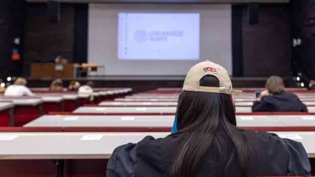 Eine Studentin mit Kappe sitzt in einem Hörsaal der Universität Wien vor einer Leinwand.
