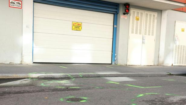 Vor einer Garageneinfahrt mit Hinweisschildern sind grüne Markierungen auf dem Asphalt zu sehen.