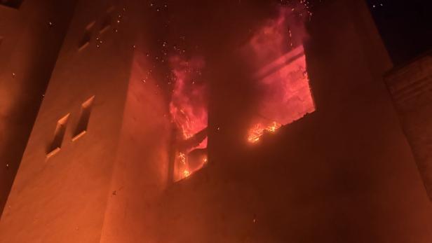 Ein Gebäude steht in Flammen, Rauch steigt auf und Funken fliegen.
