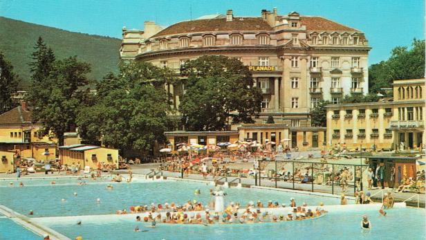 Viele Menschen baden in einem großen Freibad, im Hintergrund stehen Bäume und ein historisches Gebäude mit dem Schriftzug „PLANADE“.