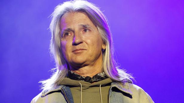 Ein Mann mit langen, grauen Haaren, einem Halstuch und einer Jeansjacke blickt nachdenklich.