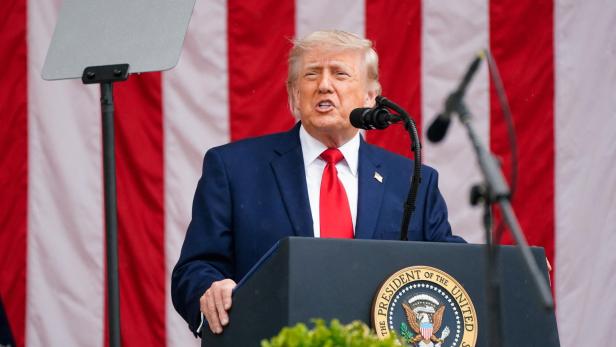 Donald Trump spricht vor einer rot-weiß gestreiften Kulisse am Rednerpult.